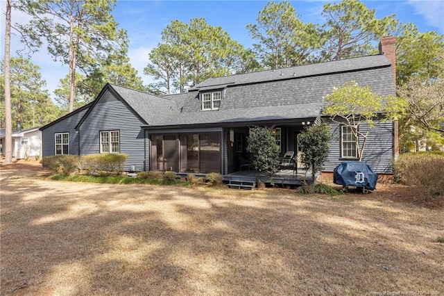 rear view of house with a sunroom, roof with shingles, and a chimney