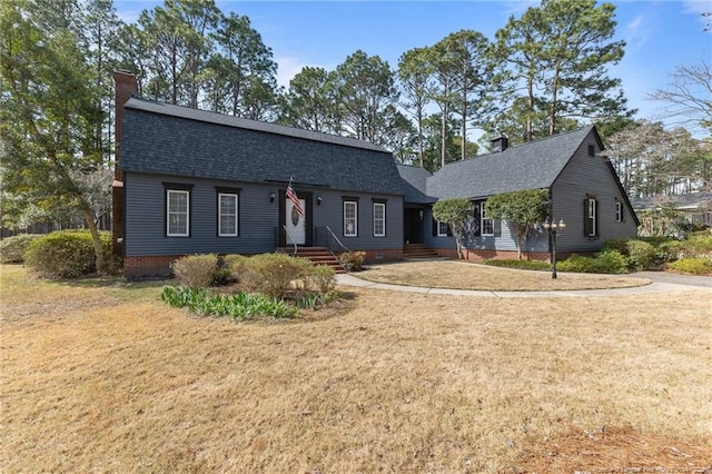 dutch colonial featuring roof with shingles, a chimney, and a front lawn