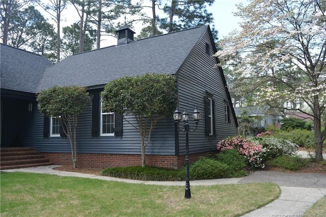 view of side of home with a chimney, a shingled roof, and a lawn