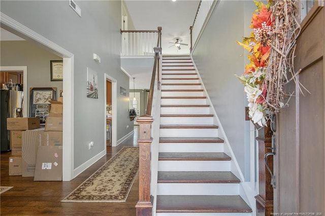 stairs featuring ceiling fan, wood finished floors, baseboards, and a towering ceiling