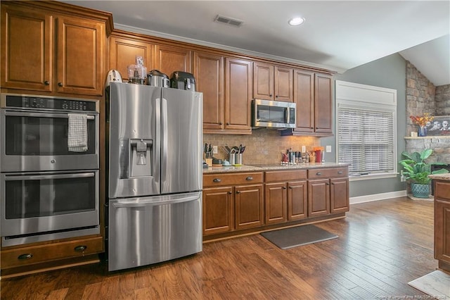 kitchen with appliances with stainless steel finishes, tasteful backsplash, baseboards, dark wood finished floors, and brown cabinets