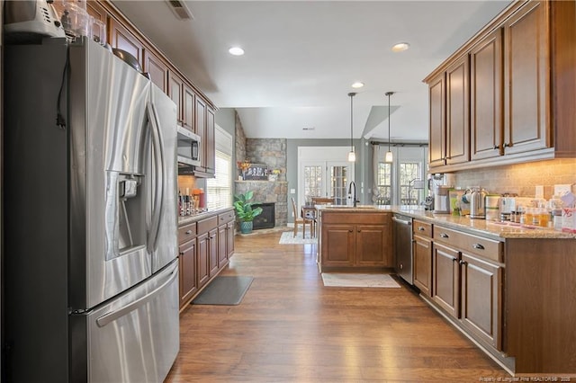 kitchen featuring appliances with stainless steel finishes, a peninsula, a stone fireplace, a sink, and backsplash