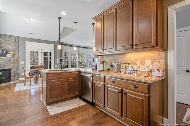 kitchen featuring stainless steel dishwasher, a peninsula, a sink, brown cabinets, and recessed lighting