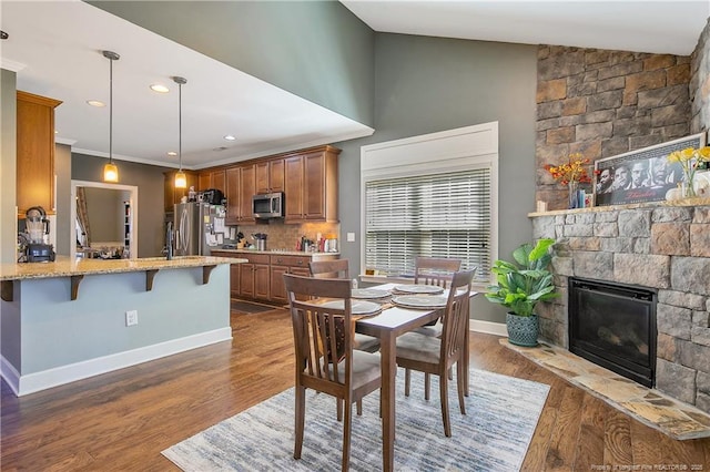 dining space featuring a fireplace, dark wood finished floors, baseboards, crown molding, and recessed lighting