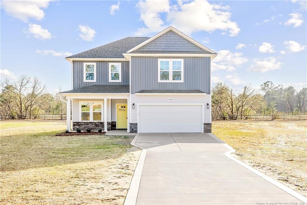 craftsman house featuring a front yard, an attached garage, stone siding, fence, and concrete driveway