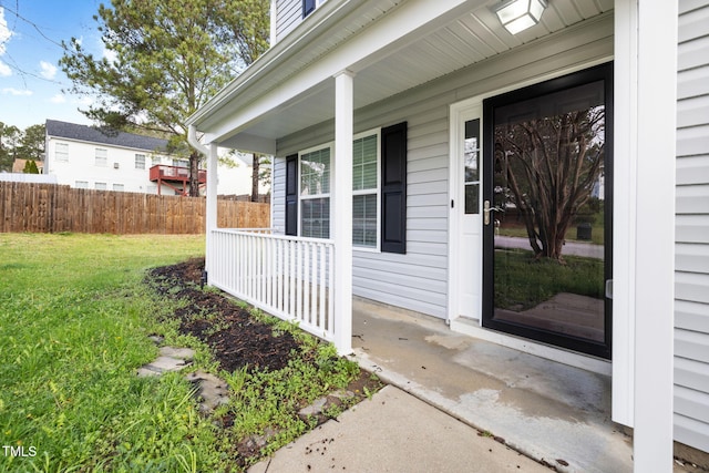 view of exterior entry featuring fence, a porch, and a yard