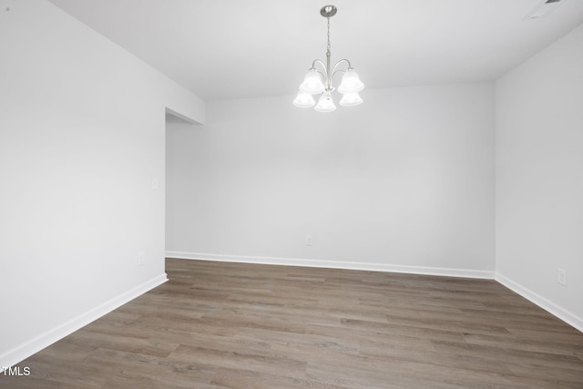 empty room featuring baseboards, visible vents, wood finished floors, and a chandelier