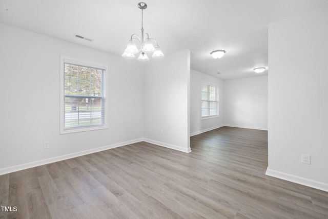 unfurnished room featuring wood finished floors, a notable chandelier, baseboards, and visible vents