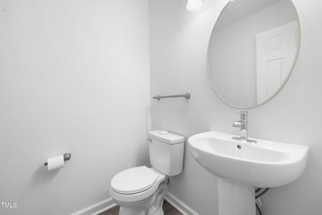 half bathroom featuring baseboards, toilet, a sink, and wood finished floors