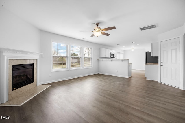 unfurnished living room with visible vents, a high end fireplace, a ceiling fan, and dark wood finished floors