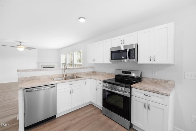 kitchen with a sink, appliances with stainless steel finishes, a peninsula, light wood-style floors, and ceiling fan