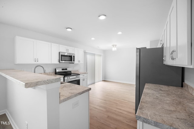 kitchen featuring light countertops, white cabinetry, appliances with stainless steel finishes, a peninsula, and light wood-style flooring