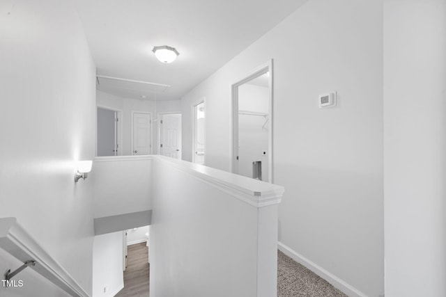 hall featuring baseboards, an upstairs landing, and attic access
