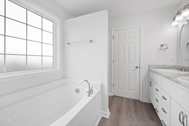 bathroom featuring a bath, baseboards, double vanity, wood finished floors, and a sink