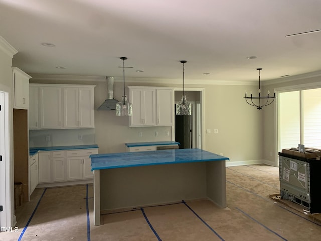 kitchen featuring wall chimney range hood, white cabinets, a kitchen island, ornamental molding, and decorative light fixtures