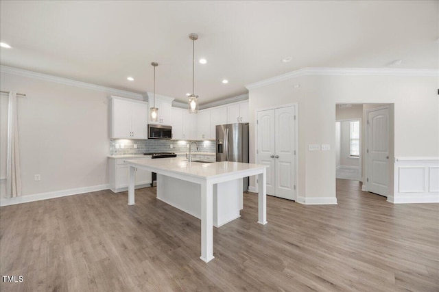 kitchen featuring stainless steel appliances, light countertops, ornamental molding, a kitchen bar, and white cabinetry