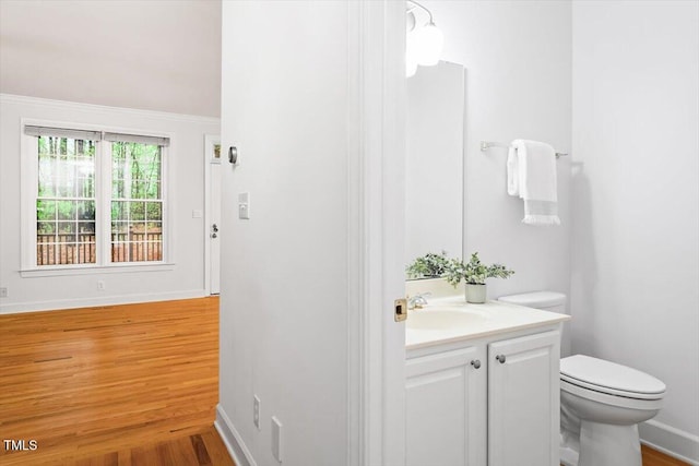 half bath featuring toilet, vanity, wood finished floors, and baseboards