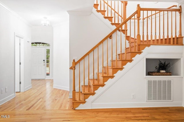 stairway featuring wood finished floors, ornamental molding, and baseboards