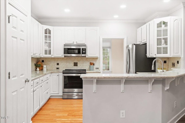 kitchen with stainless steel appliances, a peninsula, a breakfast bar, light stone countertops, and crown molding
