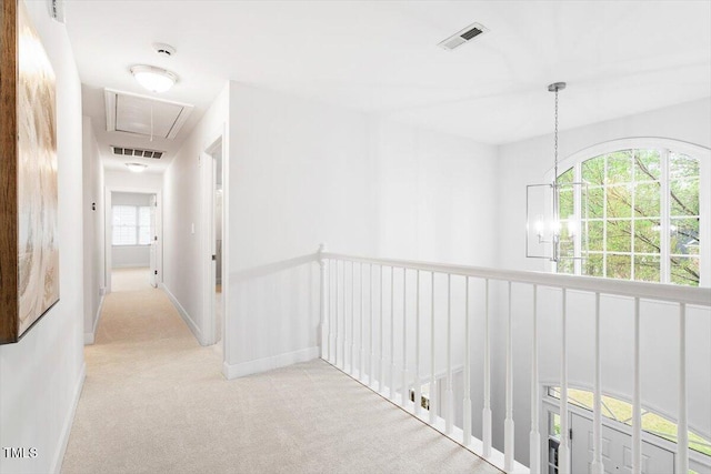 corridor with attic access, carpet flooring, baseboards, and a chandelier