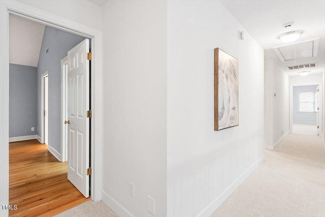 corridor featuring attic access, baseboards, and light wood finished floors