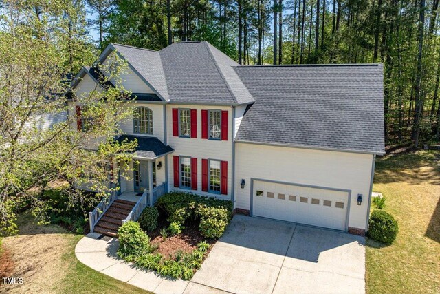 colonial inspired home with concrete driveway, an attached garage, a shingled roof, and a front yard