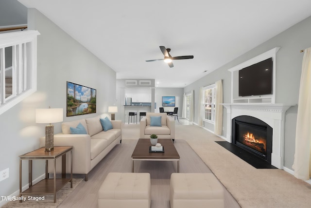 living area with a fireplace with flush hearth, wood finished floors, baseboards, and ceiling fan