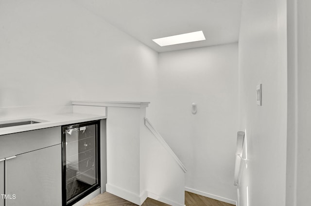 staircase with a skylight, wood finished floors, baseboards, and beverage cooler