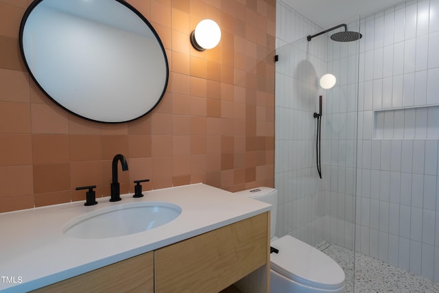 full bathroom with a tile shower, tile walls, vanity, and toilet