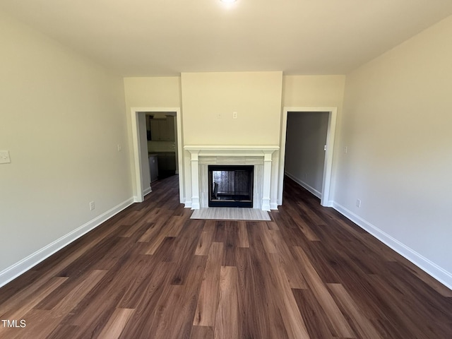 unfurnished living room with a fireplace with flush hearth, baseboards, and dark wood finished floors