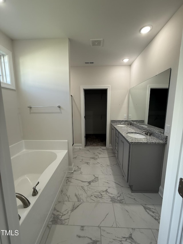 bathroom featuring a bath, visible vents, marble finish floor, a sink, and double vanity