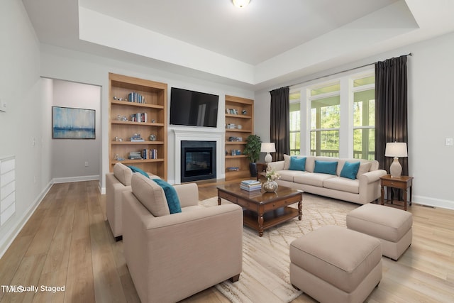 50 Gadwall Ct, Zebulon, NC 27597 - living area with a tray ceiling, a glass covered fireplace, baseboards, and light wood-style flooring