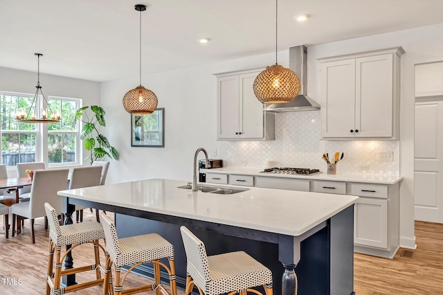 kitchen with a sink, wall chimney range hood, backsplash, and light wood finished floors