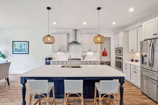 kitchen with a sink, wall chimney range hood, appliances with stainless steel finishes, and a breakfast bar
