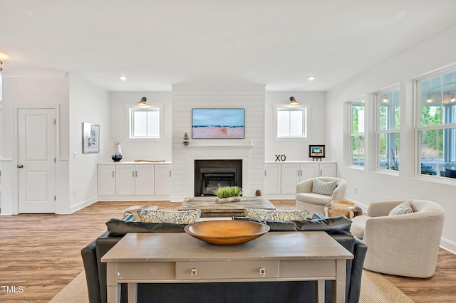 living area featuring baseboards, recessed lighting, light wood-style floors, and a fireplace