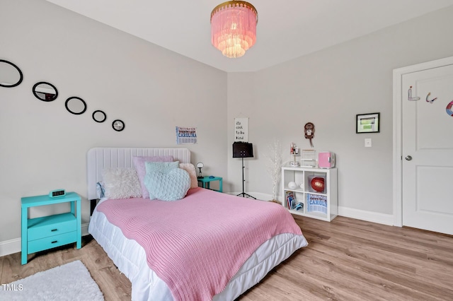 bedroom with baseboards, a notable chandelier, and wood finished floors