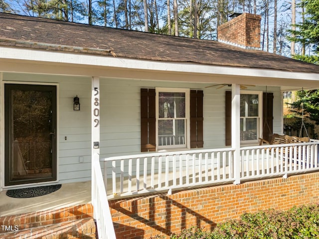 view of exterior entry with a chimney, a porch, and roof with shingles