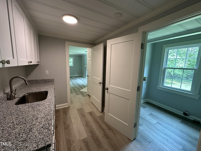 interior space featuring light stone counters, white cabinets, a sink, ornamental molding, and wood finished floors