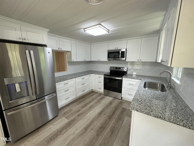 kitchen with a sink, stainless steel appliances, light wood-style floors, white cabinetry, and stone countertops