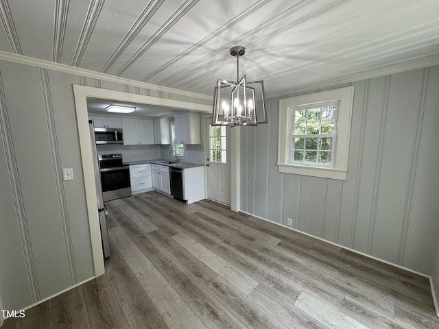 unfurnished dining area featuring crown molding, a sink, a chandelier, a decorative wall, and wood finished floors