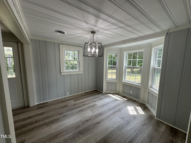 unfurnished dining area with ornamental molding, an inviting chandelier, wood finished floors, and visible vents