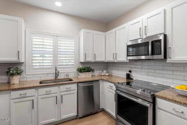 kitchen featuring white cabinets, light stone countertops, stainless steel appliances, a sink, and backsplash