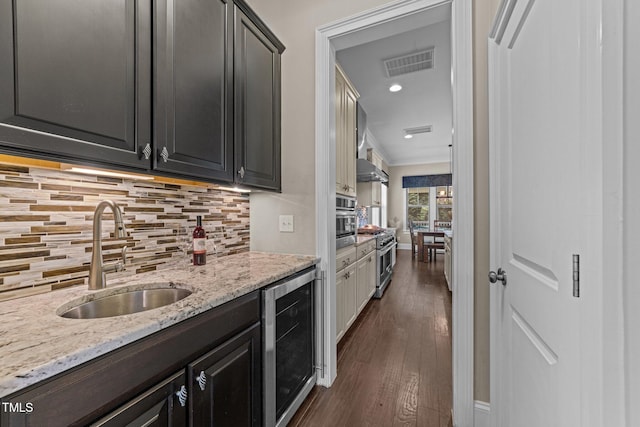 kitchen with backsplash, visible vents, a sink, light stone counters, and beverage cooler