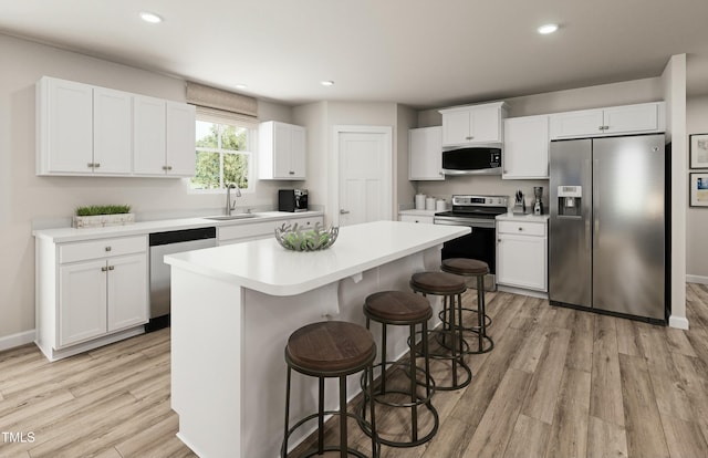 kitchen featuring a kitchen breakfast bar, light wood-type flooring, a kitchen island, a sink, and appliances with stainless steel finishes