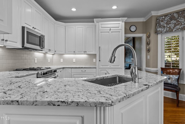 kitchen with dark wood-style flooring, white cabinets, ornamental molding, appliances with stainless steel finishes, and a sink