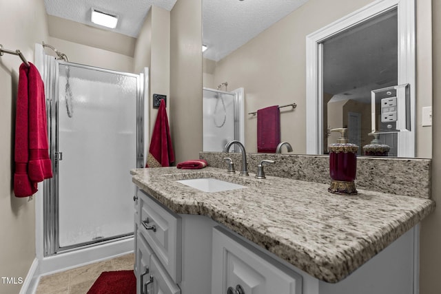full bath featuring vanity, baseboards, a textured ceiling, tile patterned floors, and a stall shower