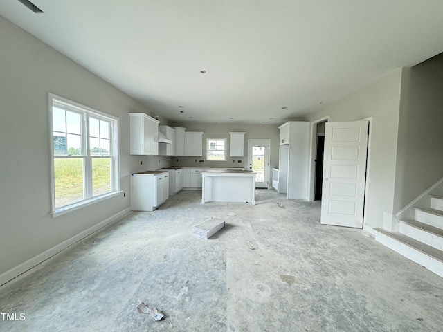kitchen with white cabinetry, a kitchen island, custom exhaust hood, and baseboards