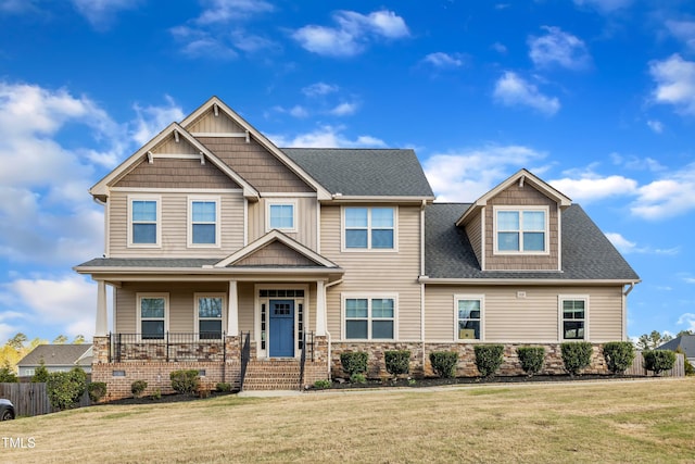 craftsman inspired home featuring a shingled roof, covered porch, a front yard, and fence