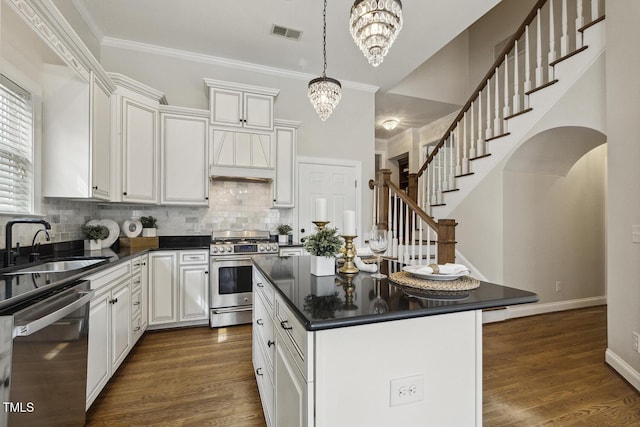 kitchen with a notable chandelier, a sink, ornamental molding, appliances with stainless steel finishes, and dark countertops