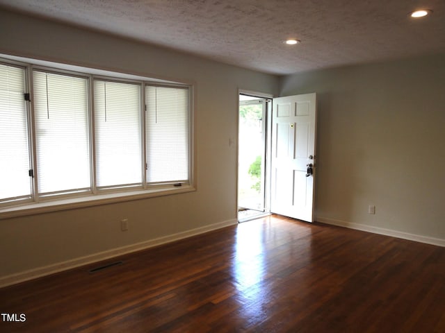 empty room featuring a textured ceiling, visible vents, baseboards, recessed lighting, and dark wood-style floors